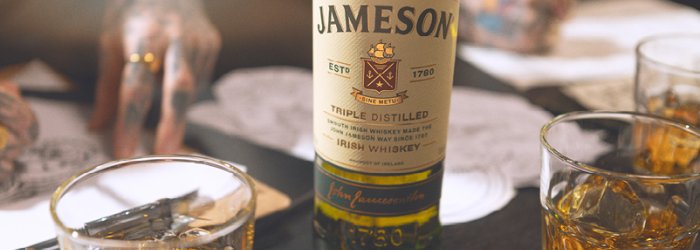 A Jameson whiskey bottle stands on a table next to filled glasses and documents.