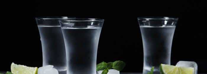 Drie glazen gevuld met wodka worden op tafel gezet met schijfjes limoen en ijsblokjes.