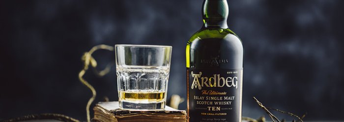 A whisky bottle and a glass stand on old books, surrounded by branches.