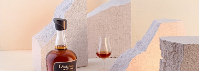 Braune Rumflasche steht auf hellem Hintergrund, umgeben von weißen, strukturierten Steinen und Glas.