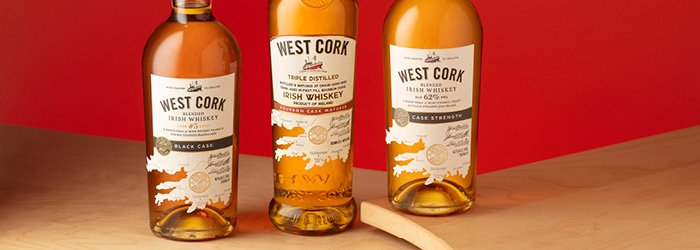 Three bottles of The Glenturret Single Malt Scotch stand on a wooden barrel stave against a red background in a horizontal shot at eye level. The bottles are arranged so that one is in the center and the others to the left and right.