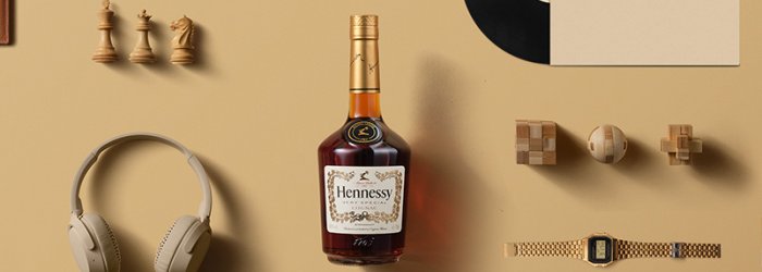 Eine Flasche Hennessy steht zentral, umgeben von Schachfiguren, Kopfhörern und Retro-Accessoires auf beigem Hintergrund.