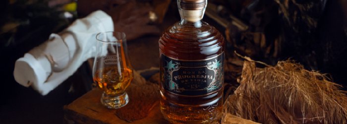 Flasche und ein Glas voll Rum auf erhöhten Holzpotest.