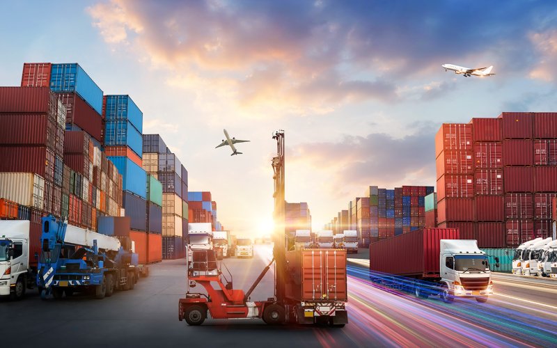 Container ships transport freight containers at sunset, with airplanes flying in the sky.