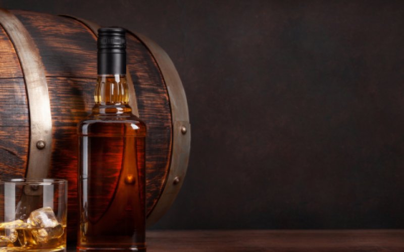 Aufnahme eines befüllten Glases. Im Hintergrund ist ein Fass zu erkennen  