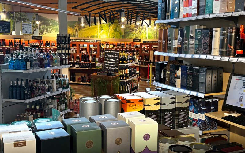 Regale präsentieren diverse Spirituosenverpackungen, umgeben von einer gemütlichen Weinladen-Atmosphäre mit hölzernen Elementen.