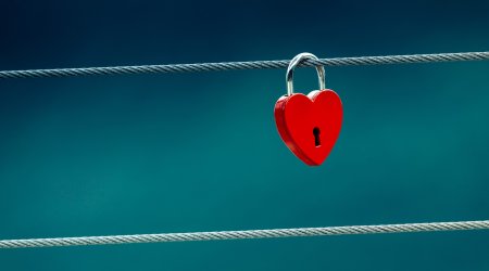 Rood hartvormig slot hangt aan een draad tegen een blauwe achtergrond.
