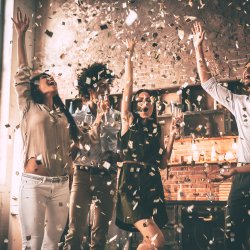 Mensen vieren feest, gooien confetti in de lucht en staan in een lichte, ruime kamer.